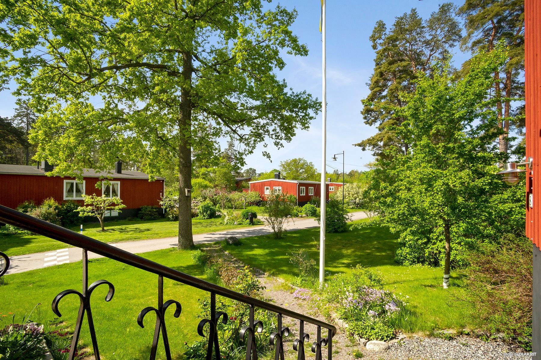 Gräsmatta, ek, smidesräcke och flaggstång